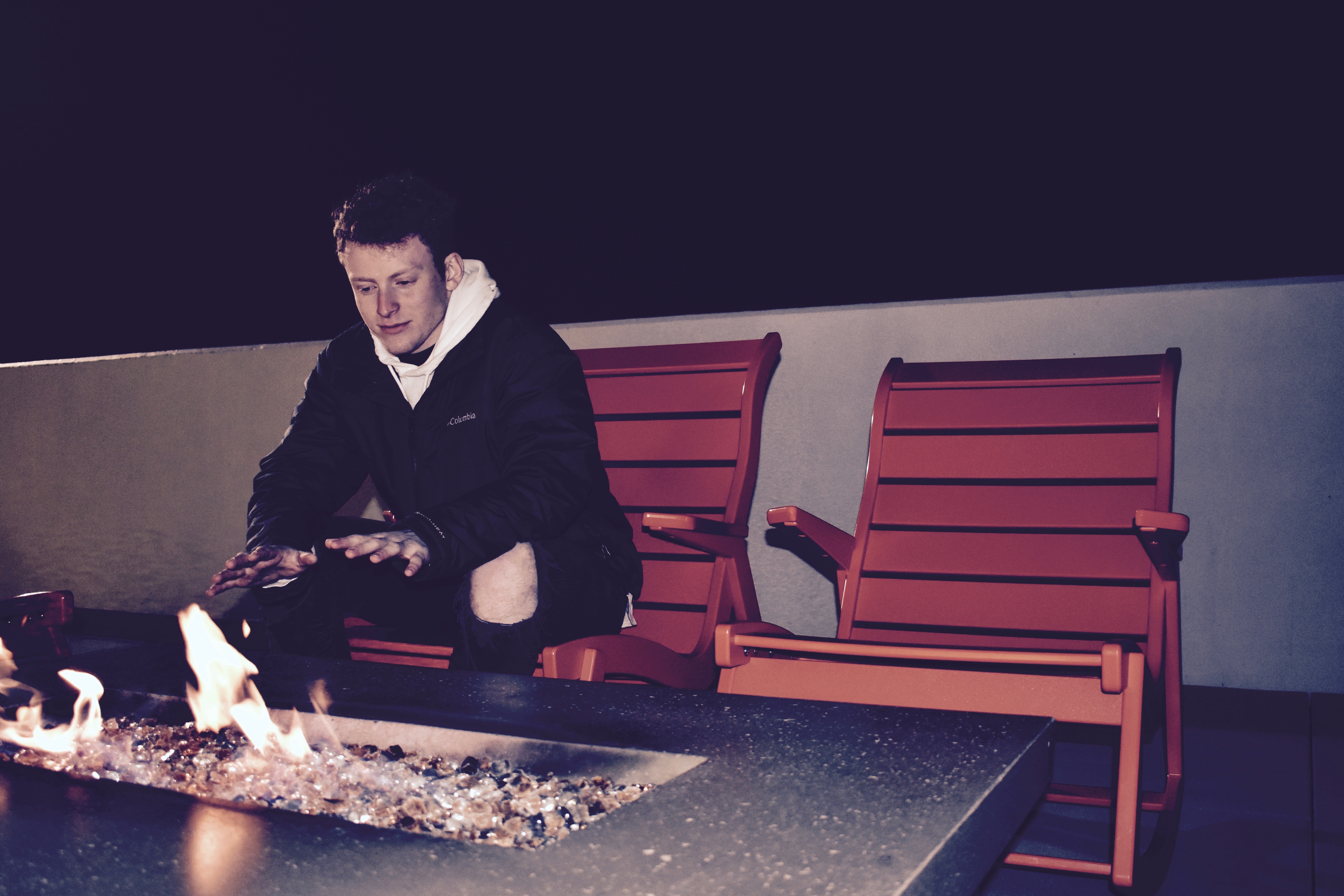 Mikey Kriegel sitting by a gas fire warming his hands